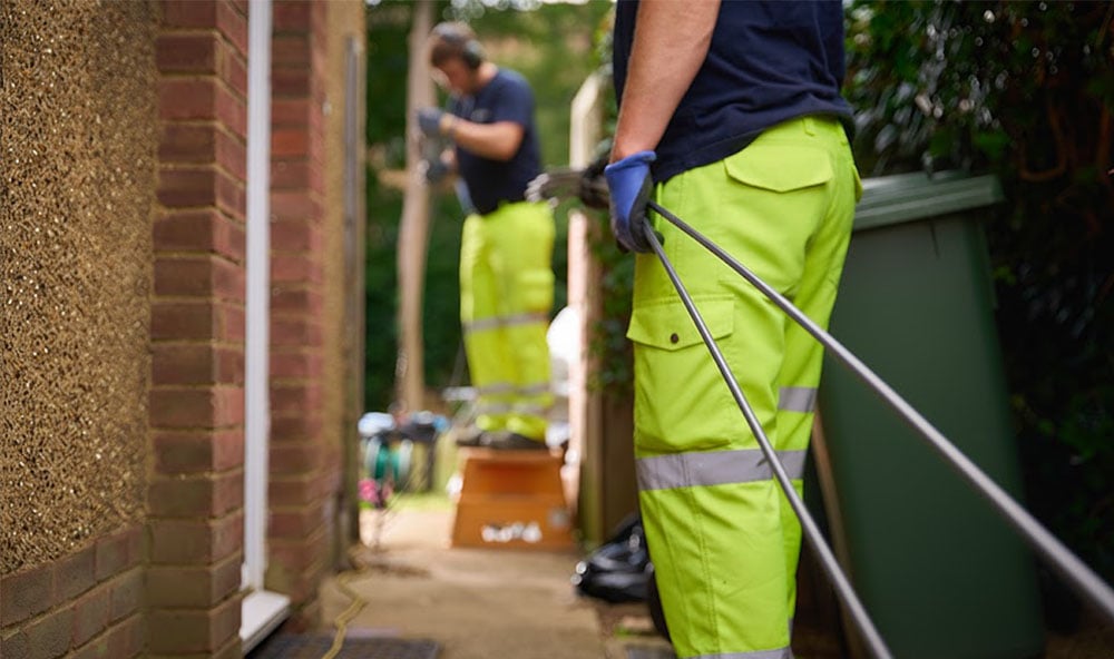 Två Geobear tekniker utför injektering vid villa iförda gula arbetsbyxor.
